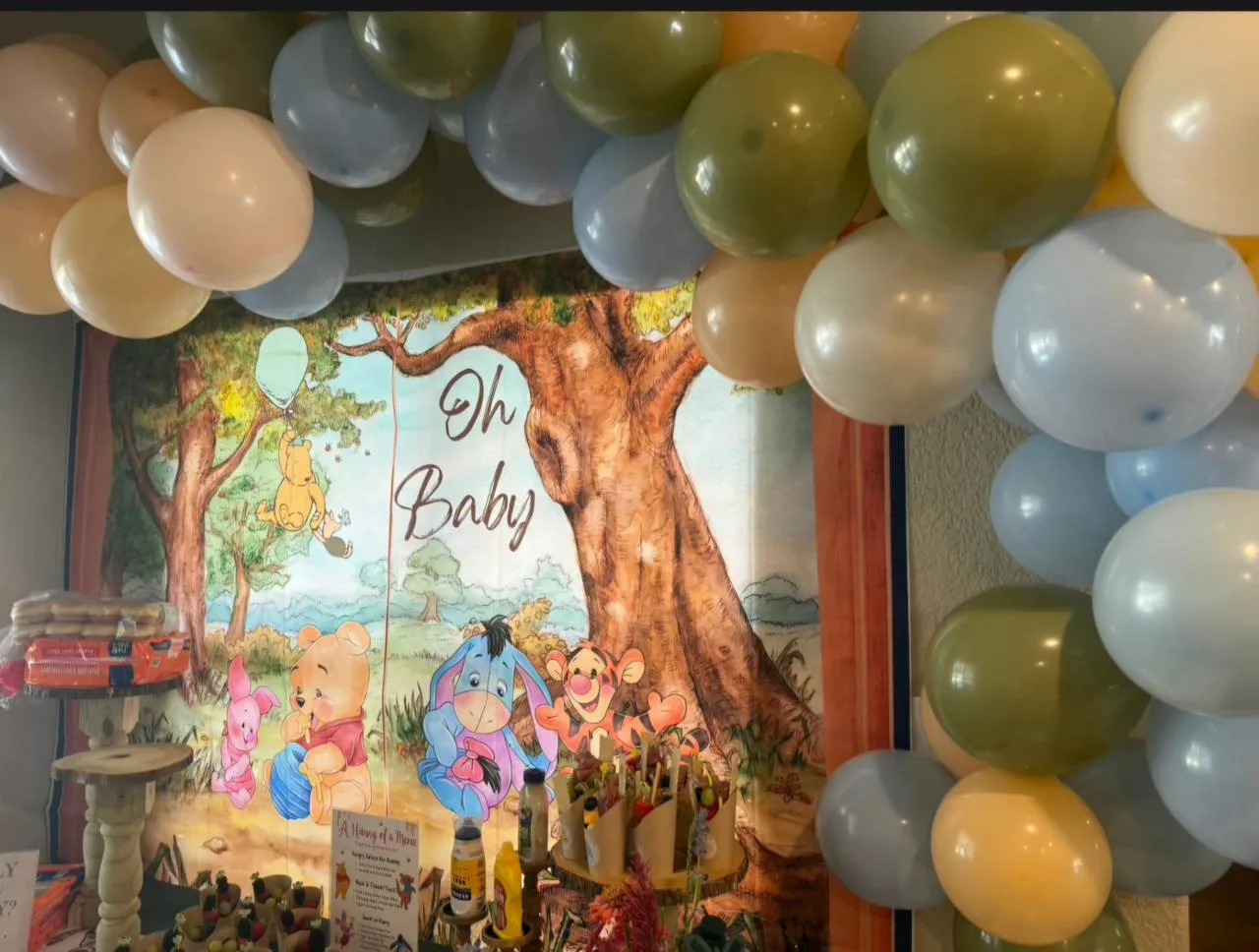 Balloon arch in olive, blue and cream around an Oh Baby woodland backdrop