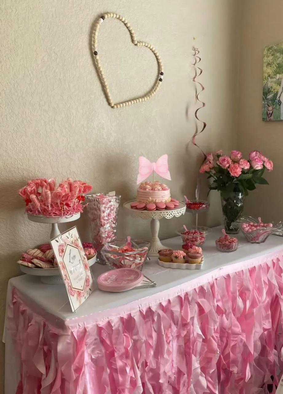 Pink ruffled dessert table with a cake, sweets and roses